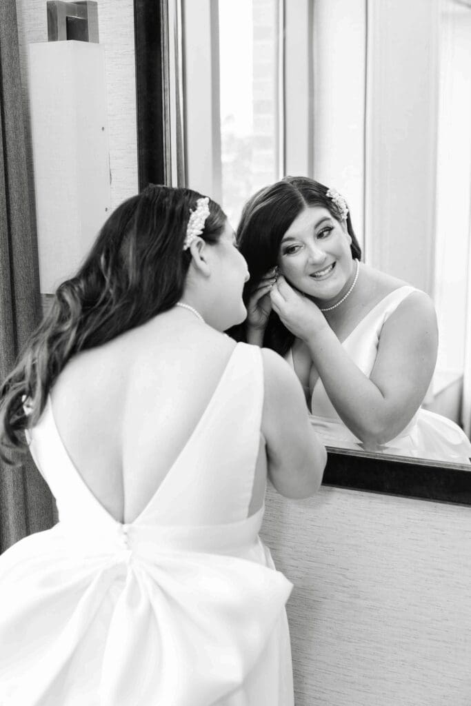 Bride getting ready for her wedding in her gown and looking in the mirror and putting on earrings at hall of springs saratoga ny.