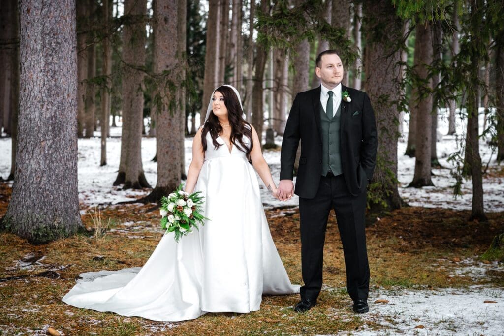 Photo by Caitlin Miller Photography of a bride and groom holding hands and posing in wedding attire surrounded by snow and trees at hall of springs saratoga ny.