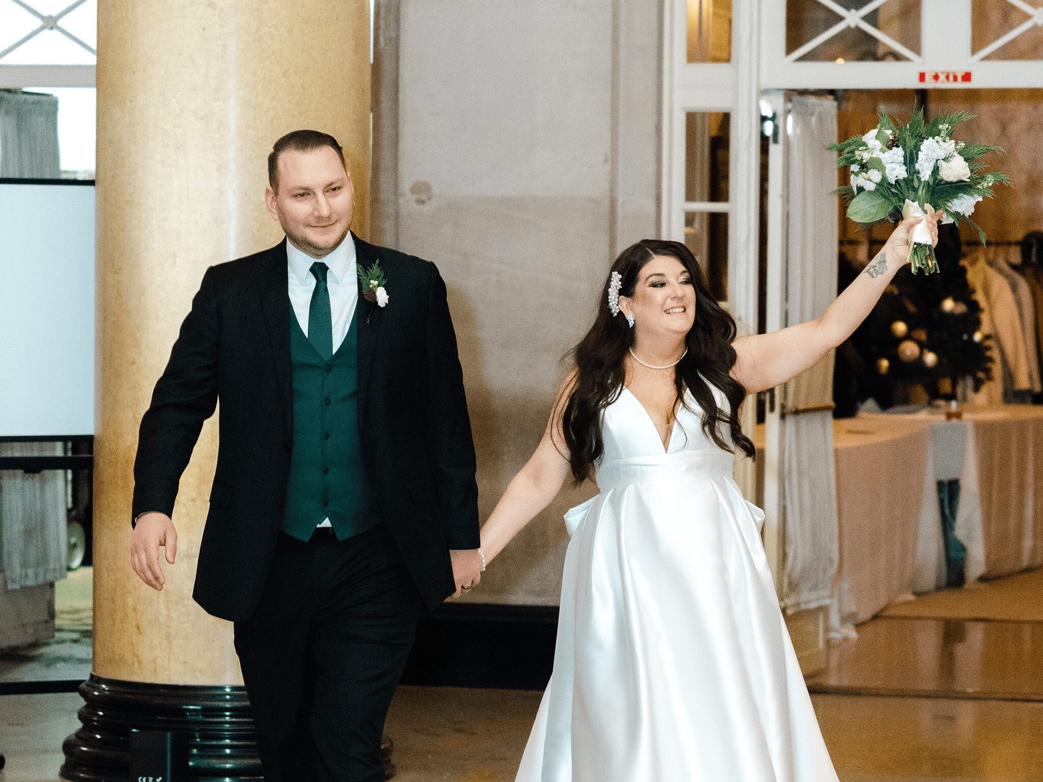 Photo of bride and groom walking into their reception celebrating their marriage with bride holding her bouquet up in the air at The Hall of Springs Saratoga NY.